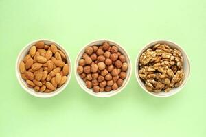 Almond, hazelnut, walnut on white ceramic bowl on green background. Healthy eating diet, nutrition, vegan concept. Protein organic food. Dry snack. National nut day. Copy space for text photo