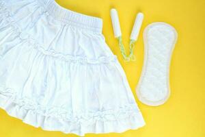 White skirt, woman sanitary pad and tampon swab on yellow background. Female menstruation cycle period. Hygiene concept. Linen and health protection idea. Copy space photo