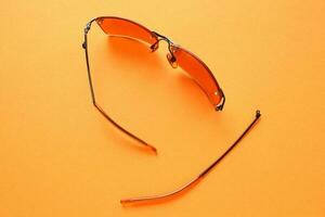 Old broken eyeglasses with damaged legs on orange background. Poor eyesight. Reuse and repair concept. Idea of health. Failure optic eyewear. Breakage of vision correction glasses. Close up, flat lay photo