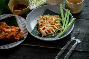 tailandés comida plato ambos en Tailandia y Asia papaya ensalada o como nosotros llamada eso somtum es complementado con A la parrilla pollo y pegajoso arroz con Fresco frituras. servido en el negro de madera mesa. foto