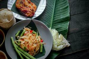 tailandés comida plato ambos en Tailandia y Asia papaya ensalada o como nosotros llamada eso somtum es complementado con A la parrilla pollo y pegajoso arroz con Fresco frituras. servido en el negro de madera mesa. foto