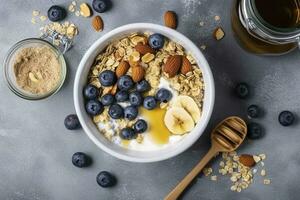 Bowl of greek yogurt with oatmeal granola, banana, blueberry, nuts, chia seeds and honey on gray table. Top view, generate ai photo