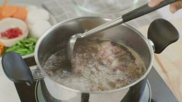 cozinhando chef mãos estão colocando carne de porco costelas dentro uma Panela do ebulição água dentro a cozinha. preparando carne de porco estoque com legumes irmão uma Panela. video