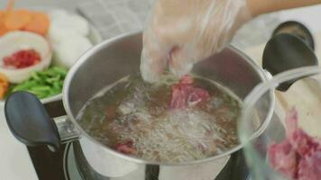 Koken chef-kok handen zijn zetten varkensvlees ribben in een pot van koken water in de keuken. voorbereidingen treffen varkensvlees voorraad met groenten bouillon een pot. video