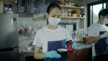 das Kaffee Geschäft weiblich Mitarbeiter ist ordentlich angezogen. stellen auf ein Maske und Handschuhe wann Gießen Kaffee zu Kunden. video