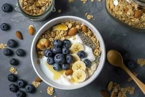 Bowl of greek yogurt with oatmeal granola, banana, blueberry, nuts, chia seeds and honey on gray table. Top view, generate ai photo