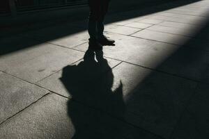 oscuro sombra de un solitario persona en el suelo en el calle. desconocido con un cigarrillo. ansiedad, depresión, soledad, temor concepto, generar ai foto