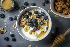 Bowl of greek yogurt with oatmeal granola, banana, blueberry, nuts, chia seeds and honey on gray table. Top view, generate ai photo