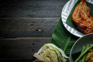 tailandés comida plato ambos en Tailandia y Asia, papaya ensalada o como nosotros llamada eso somtum es complementado con A la parrilla pollo y pegajoso arroz con Fresco frituras. servido en el negro de madera mesa. foto