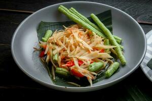 Thai food dish both in Thailand and Asia, Papaya Salad or as we call it Somtum is complemented with grilled chicken and sticky rice with fresh stir-fries. Served on the black wooden table. photo