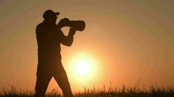 Männer nehmen draussen Bilder während szenisch Sonnenuntergang. Fotograf Silhouette. Tele Linse und das modern Kamera video