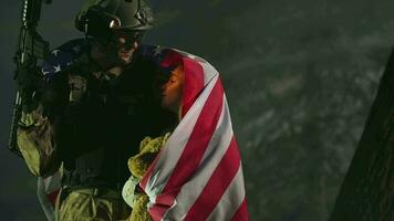 jovem criança com americano bandeira embrulhado por aí segurando Urso de pelúcia Urso e ser abraçado de pai soldado dentro cheio exército uniforme e arma dentro certo mão. video