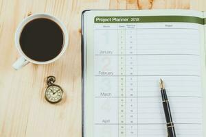 personal project planner with fountain pen and hot coffee on wood table. photo