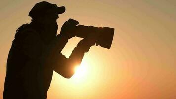 safári ao ar livre fotógrafo às pôr do sol. silhueta do homens guardando digital Câmera dentro mão com ampla telefoto lente para a Melhor animais selvagens closeups. lento movimento cenas video