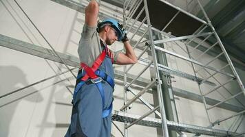 caucasico costruzione lavoratore in piedi di impalcatura mettendo su e regolazione difficile cappello controllo fibbie su imbracatura per sicurezza. video