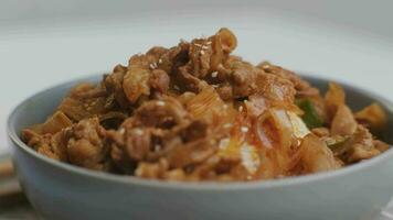 Fried kimchi with kurobuta pork on cooked rice in a bowl on wooden background. Korean food video