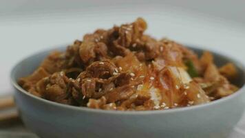 Fried kimchi with kurobuta pork on cooked rice in a bowl on wooden background. Korean food video