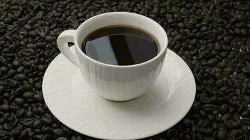 Hand holding coffee stirring spoon in white cup on table. Black coffee in white cup isolated on background of roasted coffee beans. video