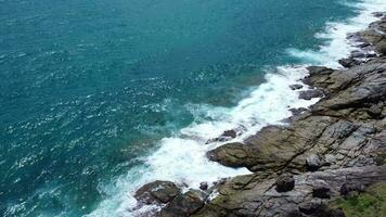 antenn se av hav vågor kraschar på stenar klippa i de blå hav. topp se av kust stenar i phuket hav. landskap se punkt av laem phromthep cape i de morgon. video