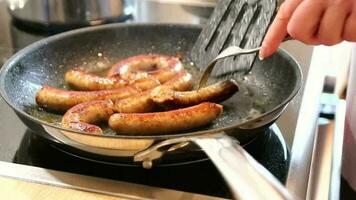 kvinna matlagning korvar i panorera på kök matlagning tallrik med gaffel och svart spatel med utsökt fet bratwurst för middag som ohälsosam men kryddad och rostad korv måltid för lunch och de barn video