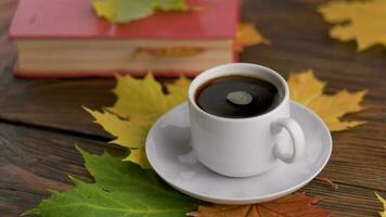 coffe cup on wooden table with book and colorful autumnal maple leaves with spinning coffee bubbles video