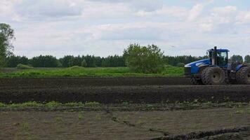 Blue New Holland tractor with double wheels pulling harrow at spring day with slow motion video