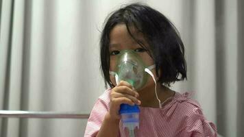 pequeño asiático niña teniendo un oxígeno máscara y respiración mediante un neutralizador a el hospital. concepto de bronquitis, respiratorio y médico tratamiento. video