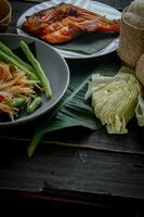 tailandés comida plato ambos en Tailandia y Asia, papaya ensalada o como nosotros llamada eso somtum es complementado con A la parrilla pollo y pegajoso arroz con Fresco frituras. servido en el negro de madera mesa. foto