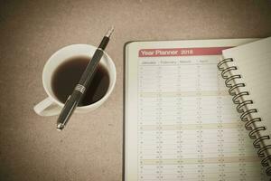 personal organizer or planner with fountain pen and hot coffee on wood table. photo