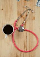 Pink stethoscope is medical instruments with hot coffee on wooden. photo