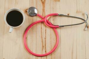 Pink stethoscope is medical instruments with hot coffee on wooden. photo