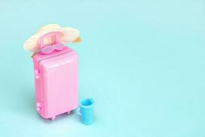 toy pink suitcase with sunglasses and a glass of soft drink on a light blue background with copy space photo