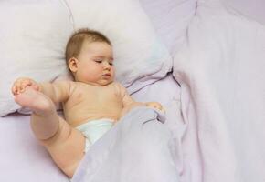 baby girl lies in bed and tries to free herself from under the covers photo