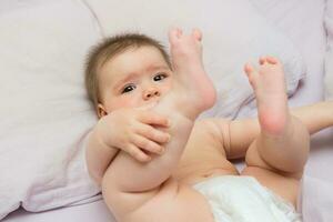 baby girl lies in bed and hold on to her legs photo