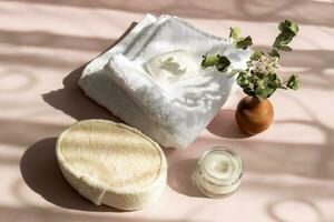 set of bath accessories in the sun with shadows, towel, washcloth, cream, soap, a bouquet of green branches in a vase photo