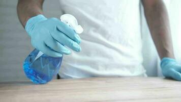 mão com luvas de borracha azul segurando frasco spray para limpar a mesa video