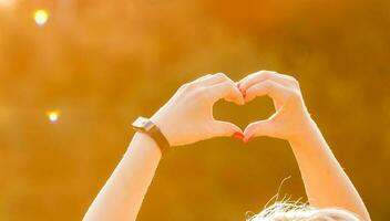 shot of heart symbol created from woman's hands over bright yellow foliage background at fine sunny autumn day. Have a good mood and be ready to fall in love at every season photo