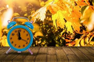 Old clock on autumn leaves on wooden table on natural background photo