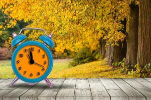 Old clock on autumn leaves on wooden table on natural background photo