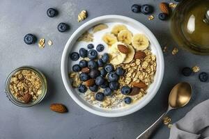 Bowl of greek yogurt with oatmeal granola, banana, blueberry, nuts, chia seeds and honey on gray table. Top view, generate ai photo