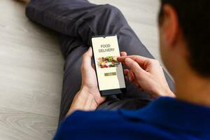 Man ordering take away food by internet with a smartphone while lying at home. photo