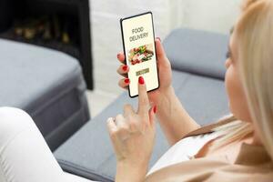 Girl ordering pizza online on smartphone, with table and coffee and plant in background photo