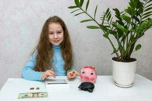a little girl spreading coins on her palm counts money on a calculator to throw into a piggy bank photo