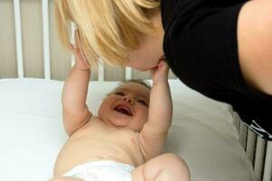 joyful baby stretches his arms to his mother leaning over the crib photo