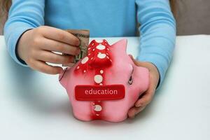 child puts a banknote in a piggy bank with the inscription education photo