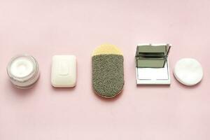 bath accessories, soap, skin sponge, cream, cotton pads, mirror on a pale pink background photo