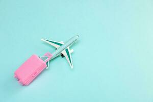 toy plane carries a pink suitcase on its tail on a light turquoise background, travel content photo