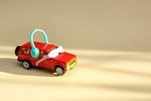 red toy car in sunglasses and headphones drives towards the sunlight on a light beige background with copy space photo