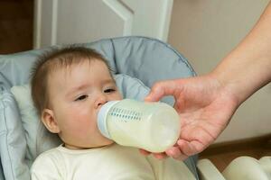 bebé niña en un alimentación silla siendo alimentado fórmula desde un botella foto