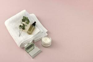 soap, towel, serum, sprig of greenery, mirror, face cream on a pale pink background with copy space photo